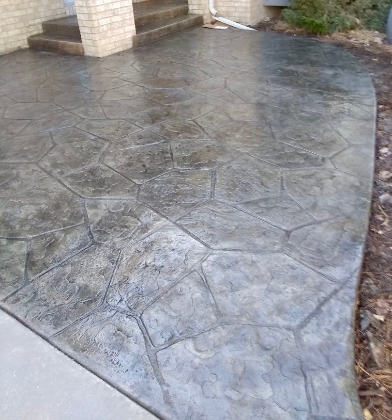 Stamped concrete patio with stone pattern next to brick house foundation