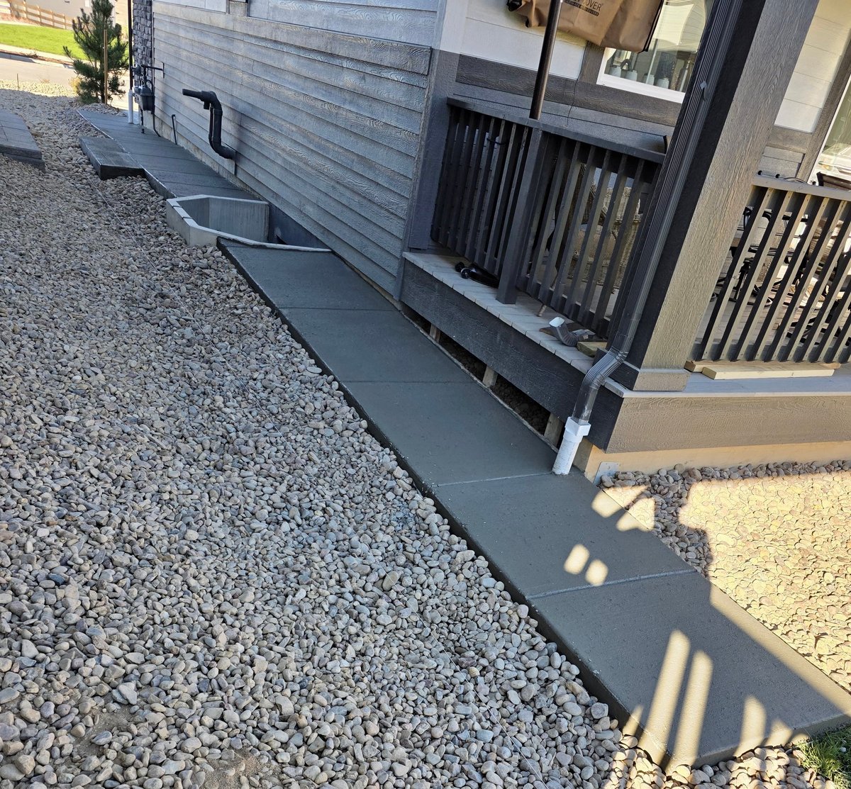 Concrete walkway along a modern house exterior with gravel landscaping and dark railings