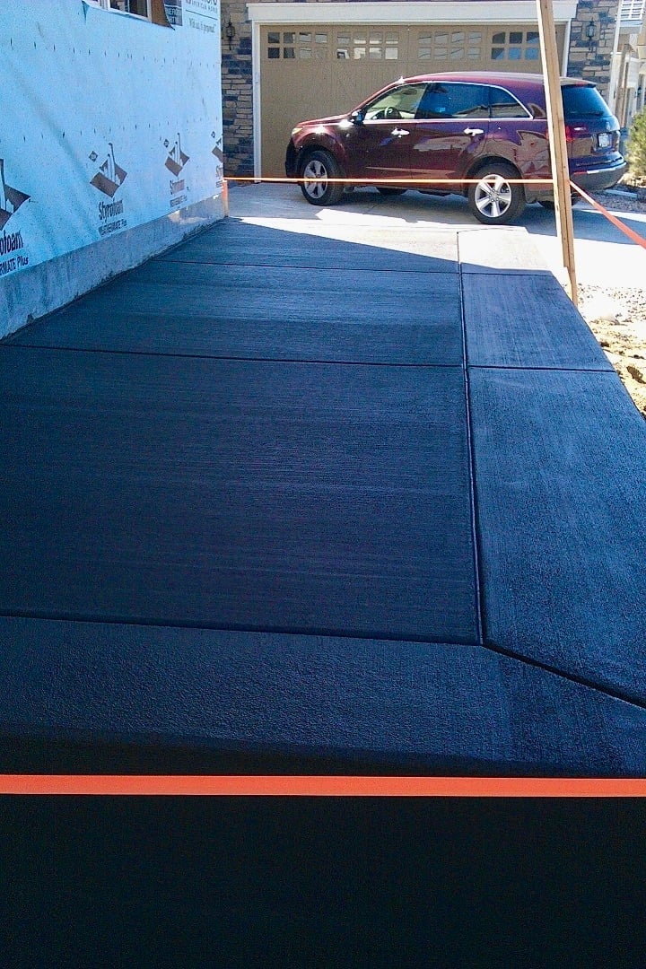 Dark blue driveway surface under construction with burgundy car and garage in background on sunny day