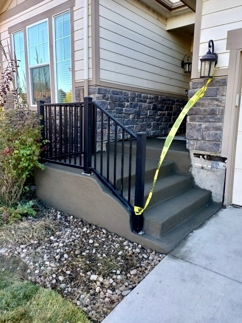 Black metal railing with yellow caution tape on concrete porch steps of house entrance