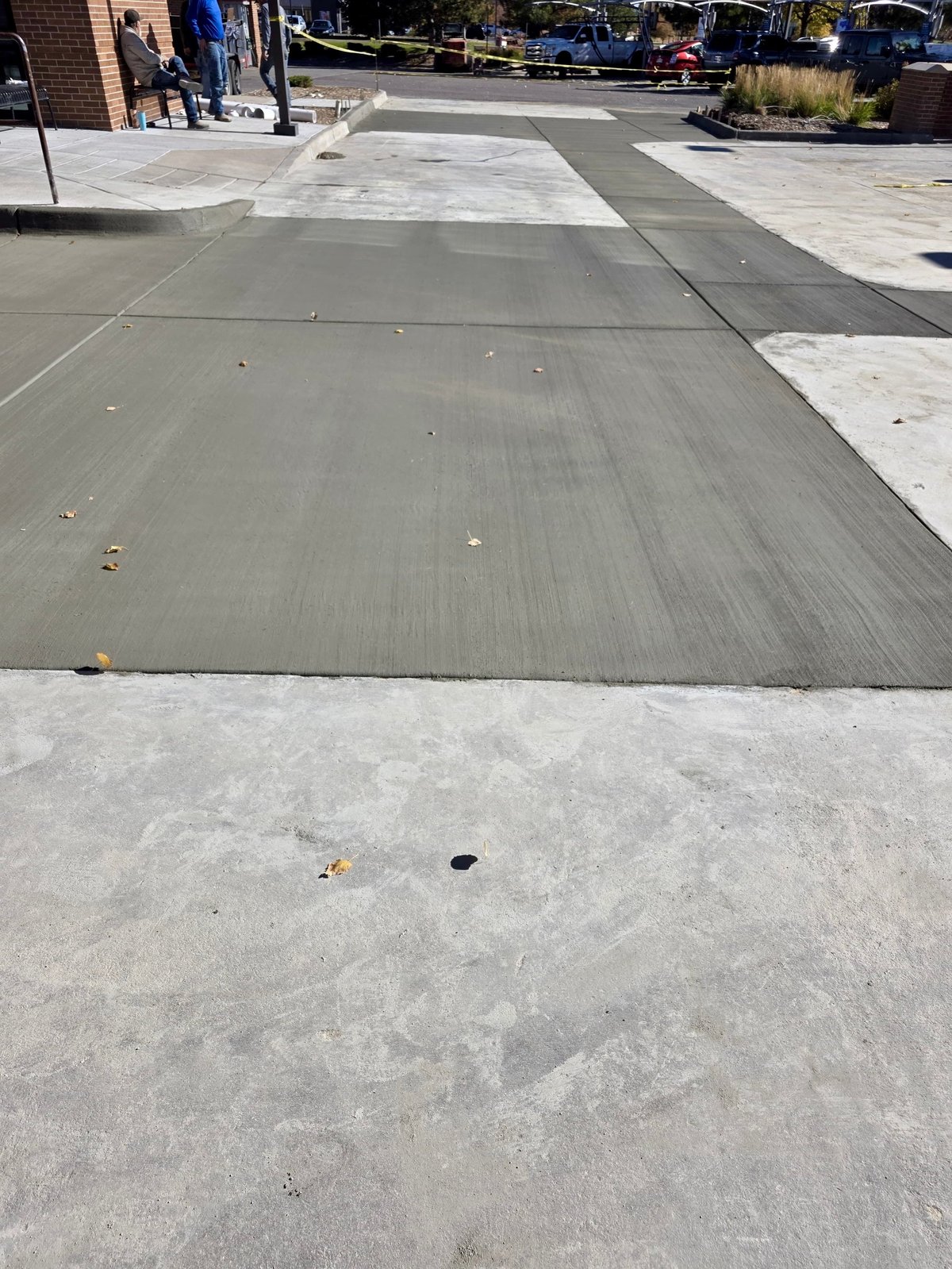 Outdoor patio or plaza with gray rubber mat pathways and light concrete pavement, brick building visible on left side