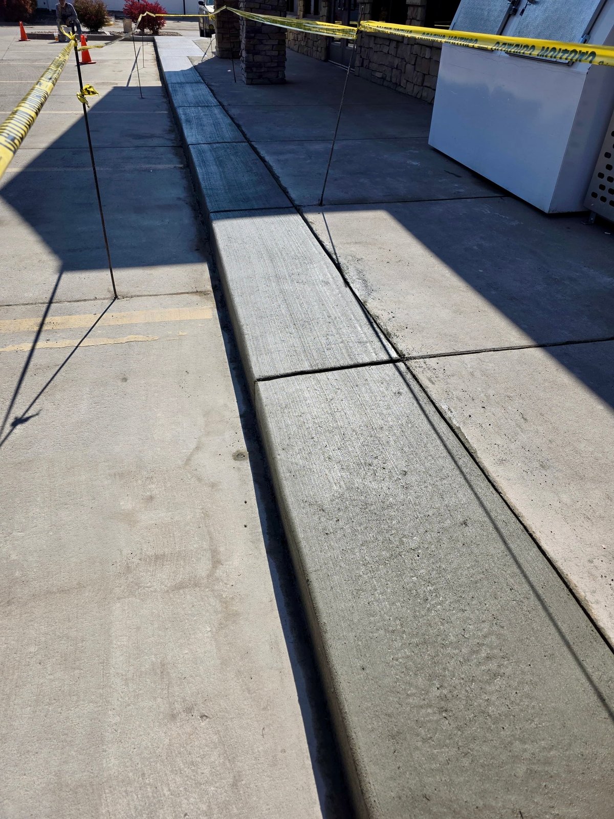 Construction site with yellow caution tape, concrete flooring, and dark tarp covering, showing ongoing building or renovation work