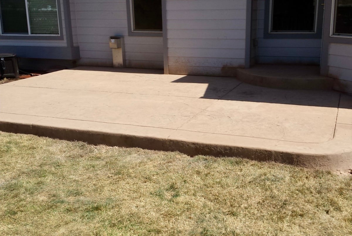 Newly poured concrete patio adjoining a brick house with patchy lawn in foreground